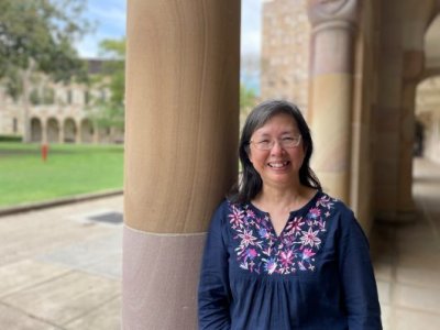Dr Poh Hillock standing outside a sandstone building with trees behind her.